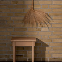 Broom with natural beige fibers against a textured yellow brick wall, above a light wooden table.