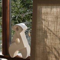 Sculptural decor in soft white against natural wood and textured beige fabric, enhancing contemporary interiors.