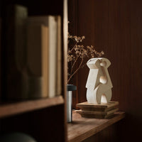 Sculptural ceramic vase in white with abstract shapes, set against a warm wood background. Sophisticated minimalist decor.