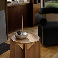 Natural wood coffee table with smooth texture; gray stone candle holder; modern dark upholstery accents.