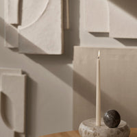 Beige and neutral decorative wall panels with a minimalist candle holder and round stone accent on a wooden table.