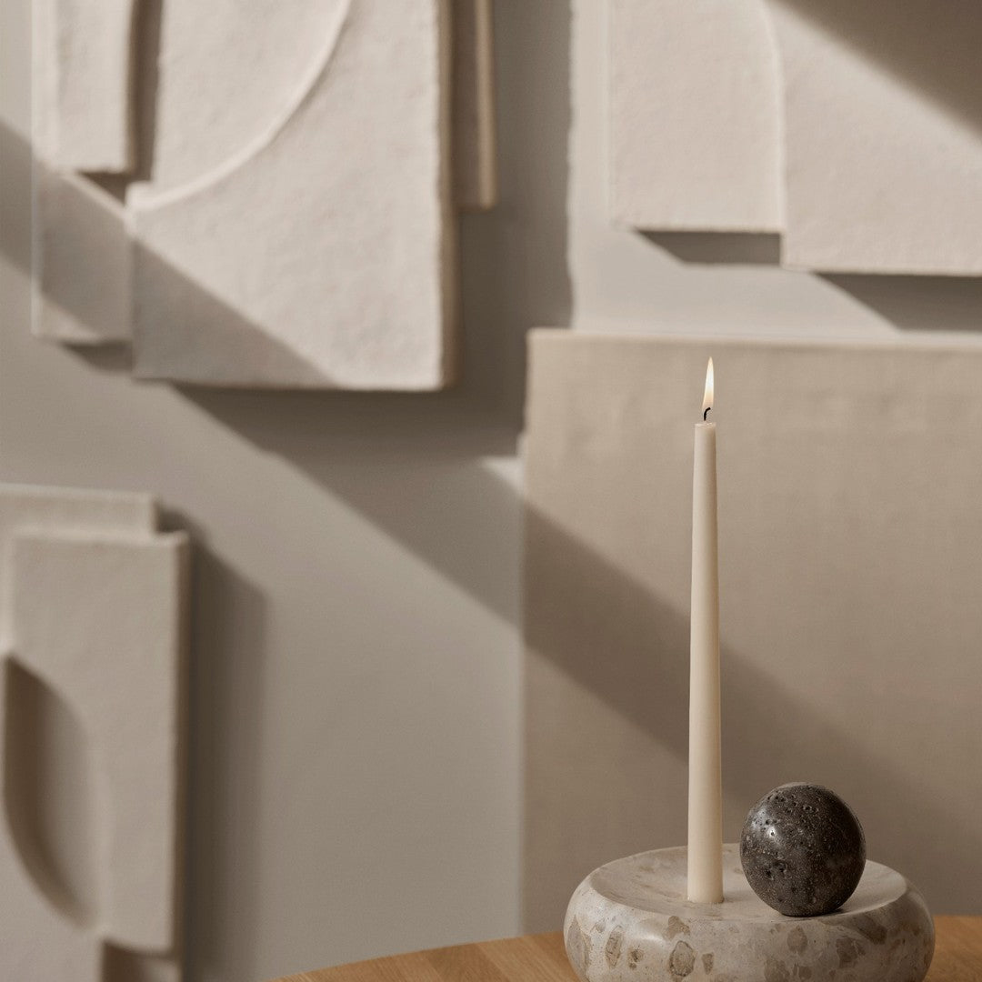 Neutral tones with soft beige textures and geometric patterns; features a slim white candle and dark round stone.