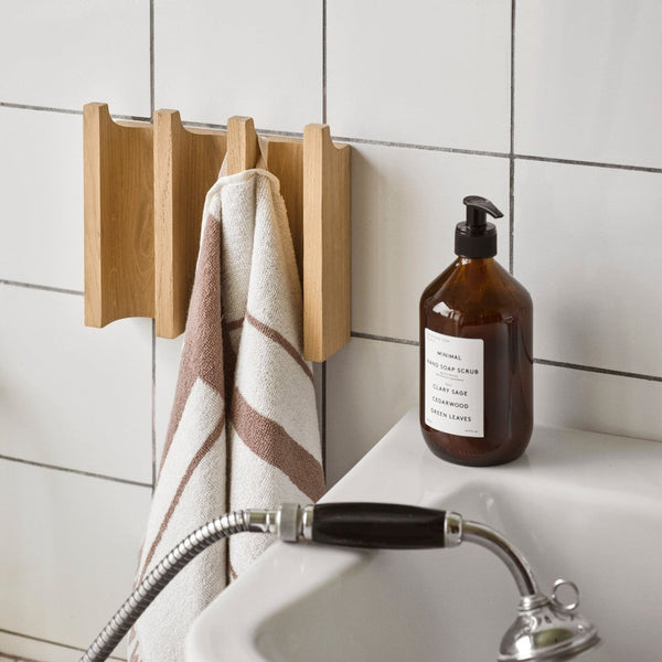 Wooden towel holder with white and brown striped towels, set against a tiled backdrop and a brown bottle.