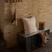 Beige and cream striped cushion on a sleek gray bench, with a round brown accent stool and muted earthy tones.