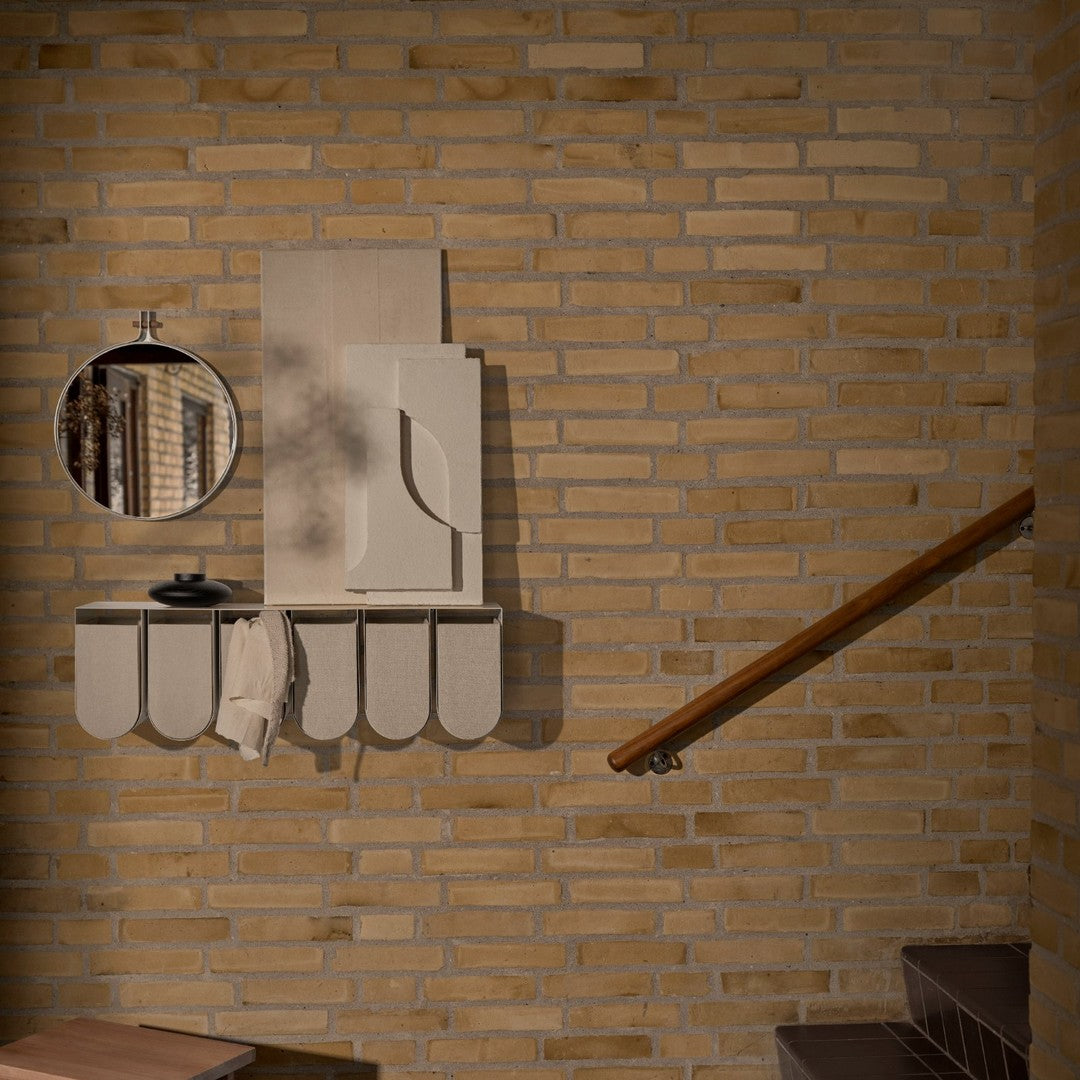 Cream and beige wall shelf with curved edges, reflecting a minimalist design against a warm, textured brick backdrop.