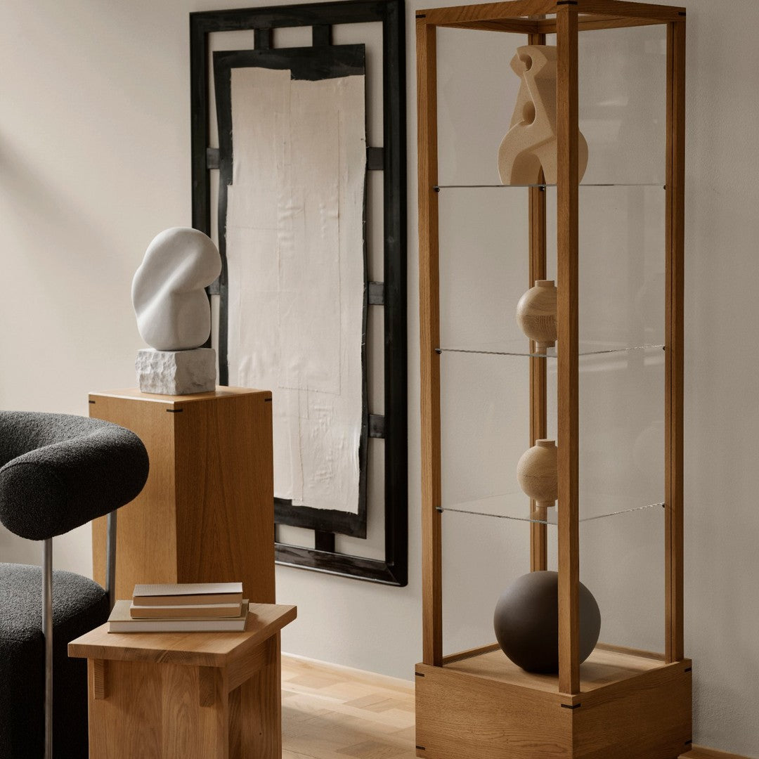 "Modern wooden display shelf featuring clear glass, neutral sculptures, and geometric patterns in a minimalist style."