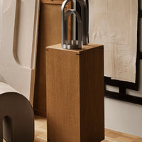 Wooden pedestal with a sleek metallic lamp, featuring warm brown tones and modern geometric patterns.