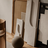Neutral-toned abstract sculptures with smooth surfaces and minimalist patterns, complemented by a round clay sphere.