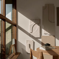 Neutral-toned wall art with geometric patterns and textured designs, complemented by warm sunlight and natural wood.