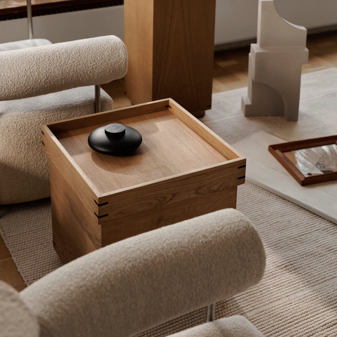 Natural wood grain with a smooth finish and a sleek black lid, set against soft beige and textured white surroundings.