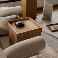 Natural wood grain with a smooth finish and a sleek black lid, set against soft beige and textured white surroundings.