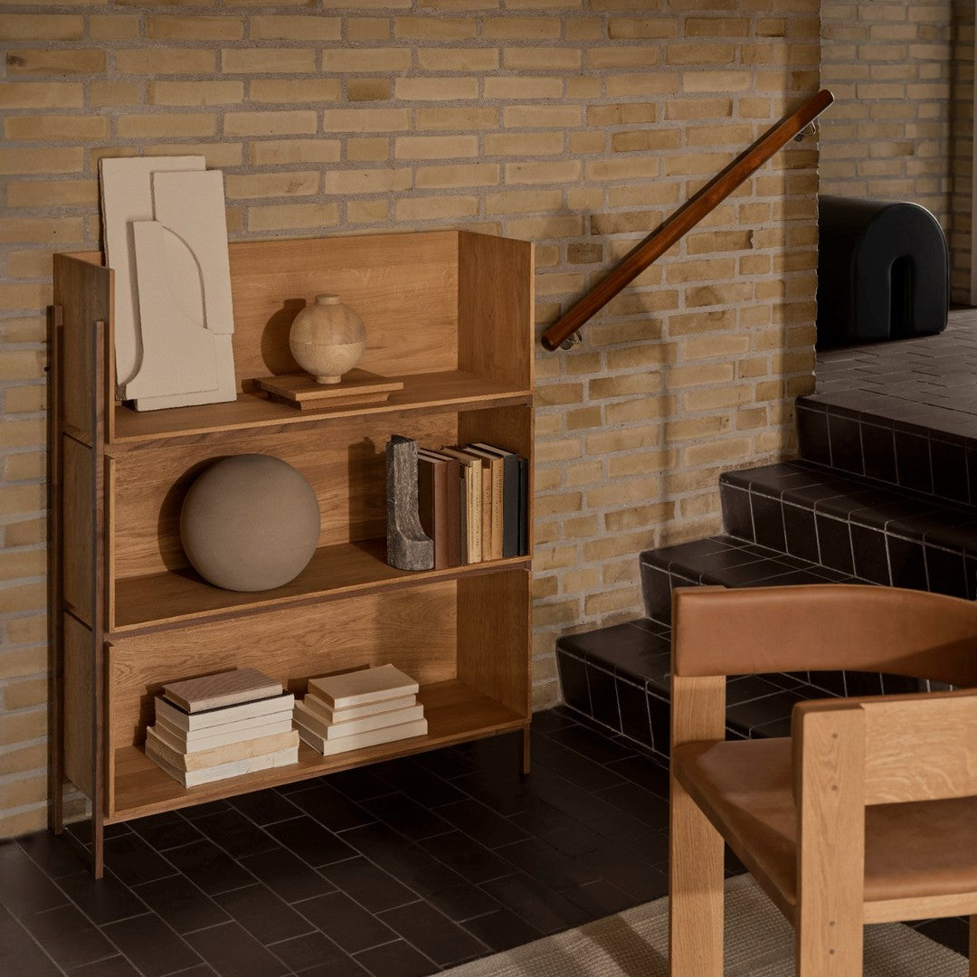 Natural wood bookshelf featuring light brown tones, paired with earthy ceramics and neutral book covers in a modern setting.