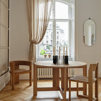 Light wood dining table with natural finish, accompanied by beige curtains and minimalistic black candle holders.