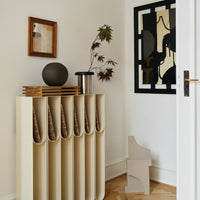 Neutral beige organizer with curved compartments, complemented by dark wood accents and a black geometric wall art piece.