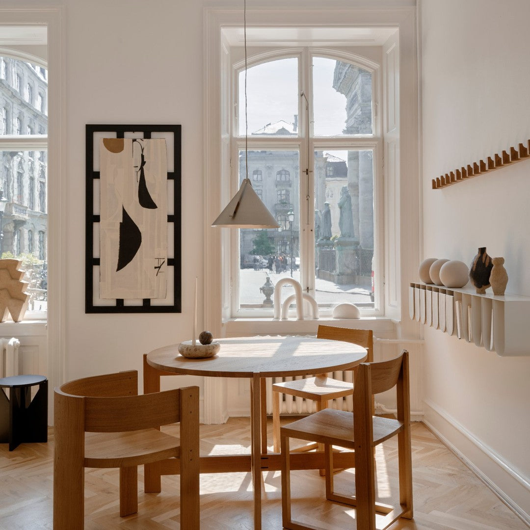 "Light wood dining set with natural tones, complemented by a black and white abstract art piece and soft beige walls."