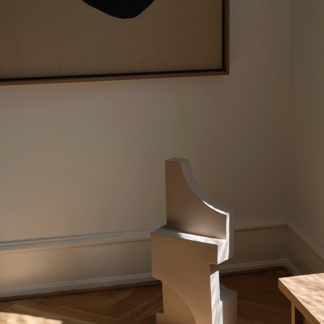 Sculptural beige decor piece with smooth curves, complementing a neutral-toned room and contrasting artwork.