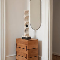 Textured white sculpture with black base, displayed on a light wood chest of drawers against a neutral backdrop.