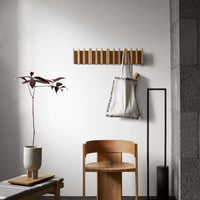 Minimalist wooden wall rack in light oak with a neutral canvas tote, accented by a burgundy plant and earthy tones.
