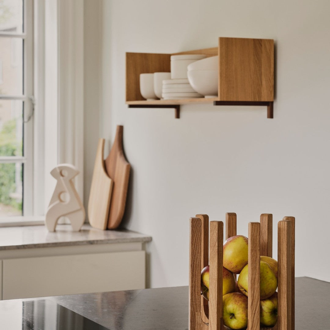 Wooden wall shelf with white bowls, beige table, and a modern fruit holder featuring vibrant green apples.