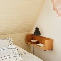 Wooden wall shelf with a warm finish, paired with white and black striped bedding against a soft cream background.