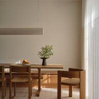 Wooden dining table with natural finishes, simple black vase, and green foliage, complemented by light neutral walls.