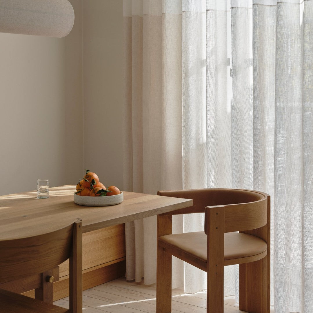 Light cream curtains with a subtle texture, wooden table and chair in natural tones, creating a warm, inviting ambiance.