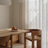 Light cream curtains with a subtle texture, wooden table and chair in natural tones, creating a warm, inviting ambiance.