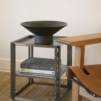 Black ceramic bowl atop a minimalist steel and wood side table, featuring a neutral color palette with textured patterns.