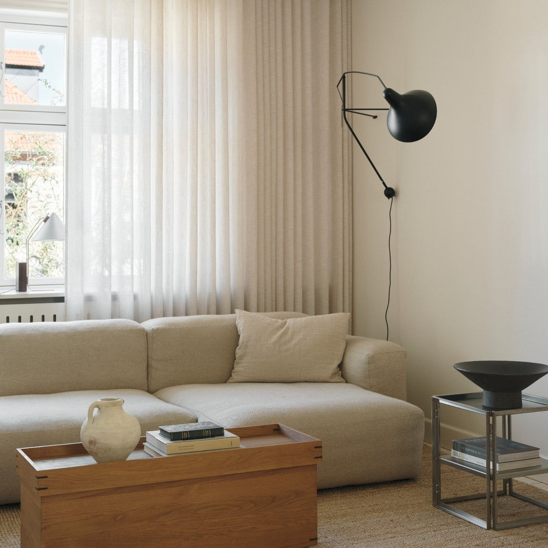 Neutral beige sofa with soft fabric, wooden coffee table, black accents, and sheer light curtains in a cozy interior.