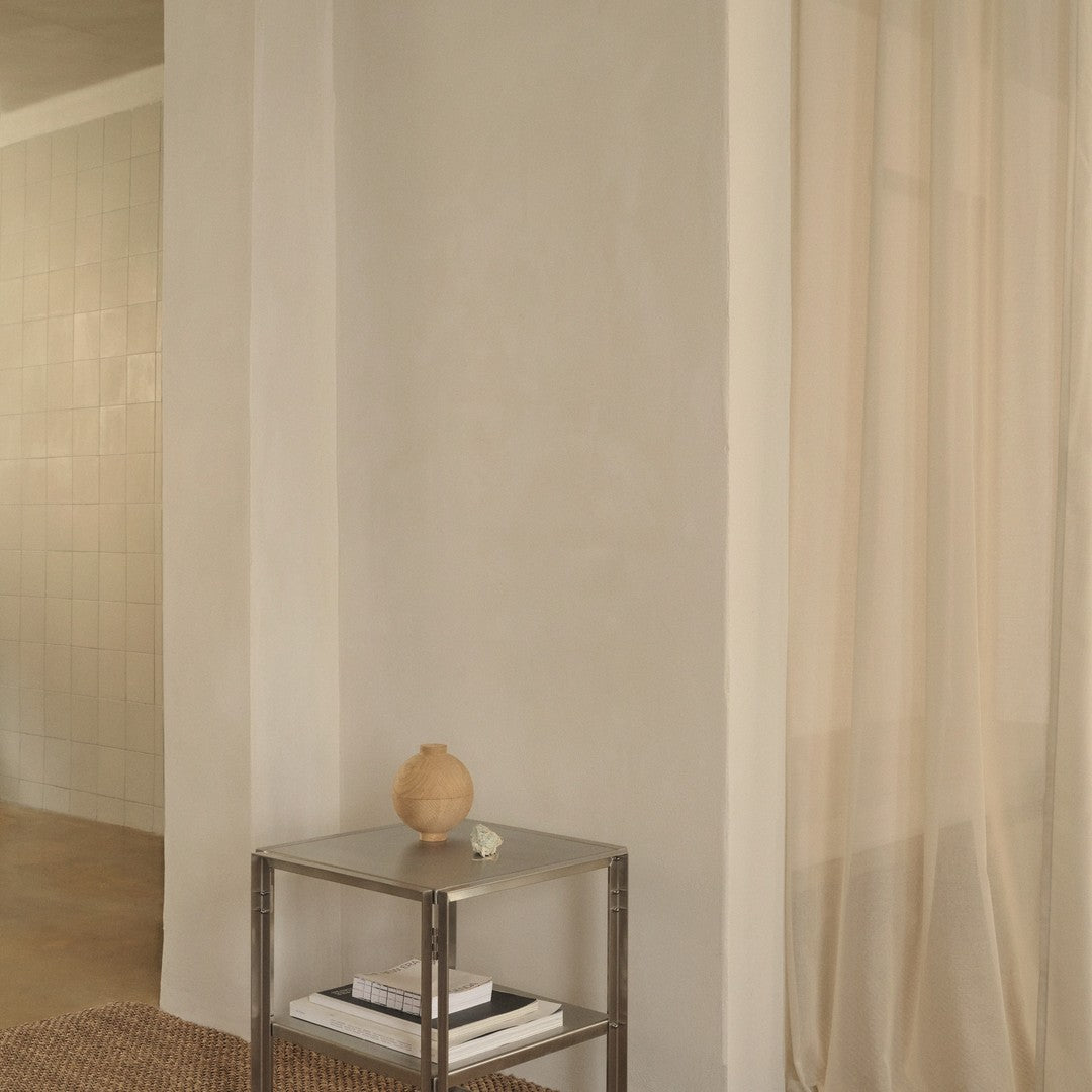 Light beige curtains drape softly, contrasting with a sleek metallic side table and warm-toned decor accents.