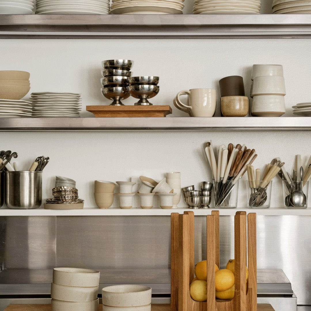 Neutral-toned dishware in varied shapes, with shiny metallic accents and natural wooden displays for a modern kitchen aesthetic.