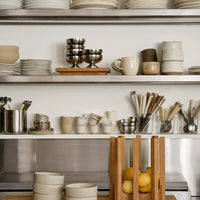 Neutral-toned dishware in varied shapes, with shiny metallic accents and natural wooden displays for a modern kitchen aesthetic.
