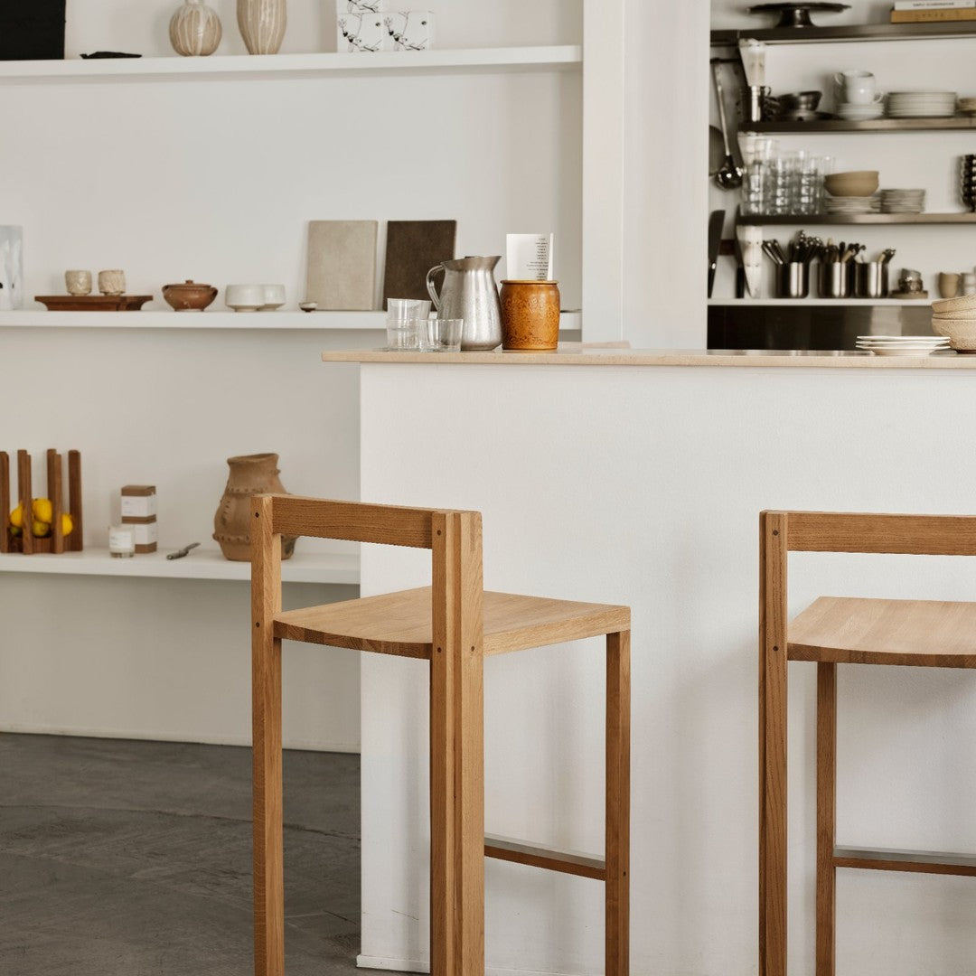 Wooden bar stools with a natural finish, set against a neutral-toned background of minimalist decor and earth-toned accents.