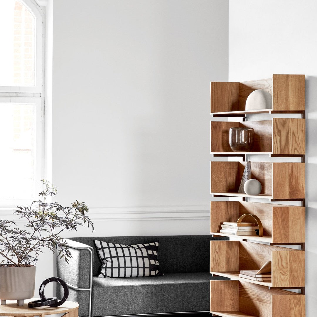 Light wood bookshelf with open compartments, set against a bright, minimalistic gray and white living room.