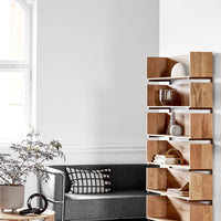 Light wood bookshelf with open compartments, set against a bright, minimalistic gray and white living room.