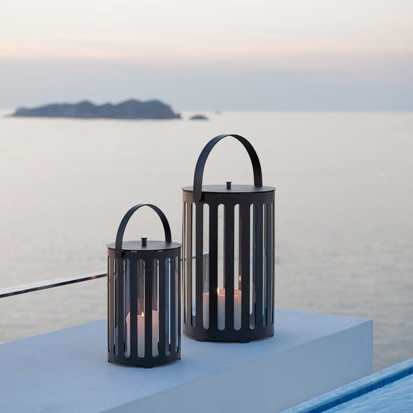 Black metal lanterns with vertical slats, set against a serene ocean backdrop at dusk.