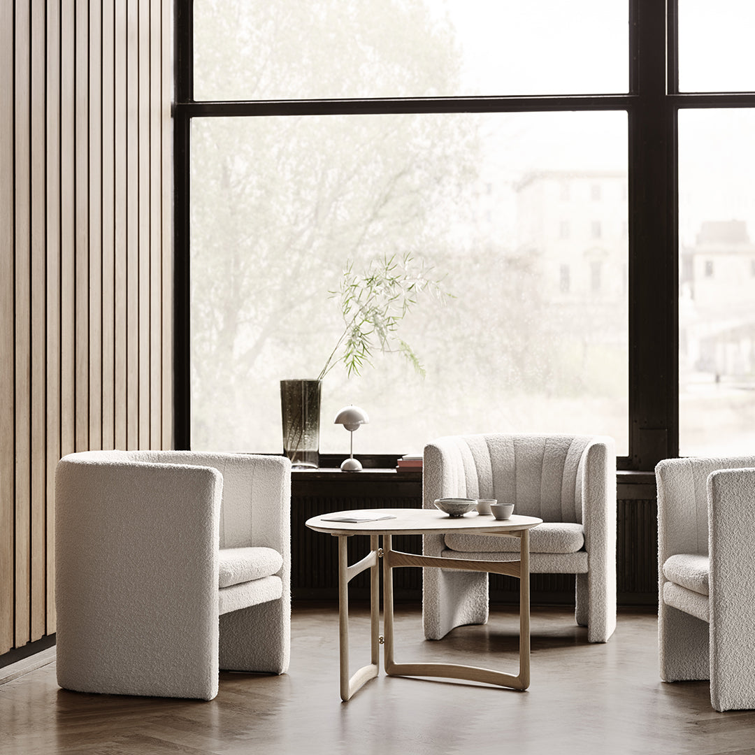 Elegant white upholstered chairs with soft texture, paired with a minimalist wooden coffee table in a bright, airy setting.