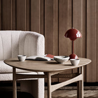 "Cozy living room scene featuring a textured cream armchair, warm wooden table, and red lamp against a brown backdrop."