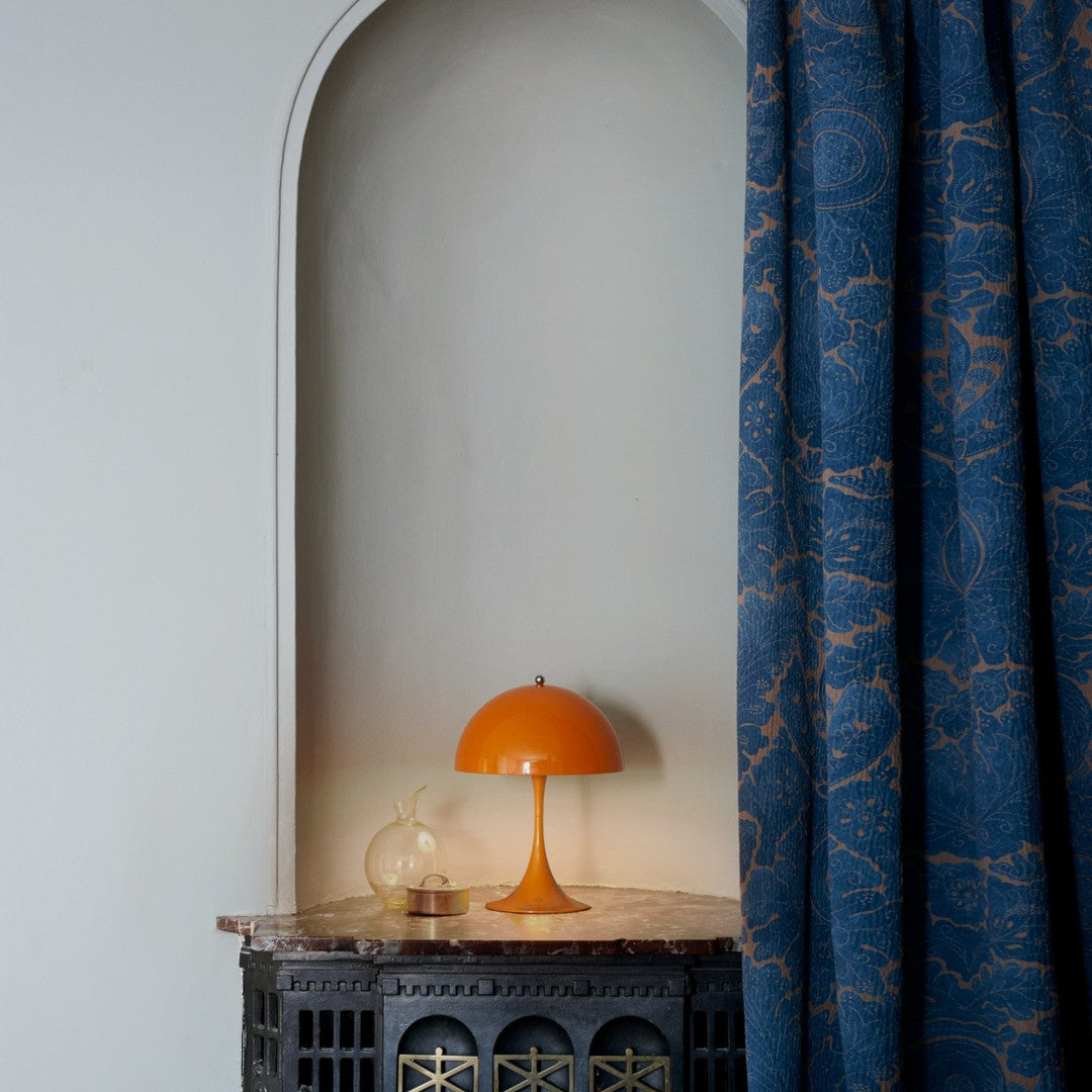 Orange Panthella lamp on a marble table against a blue curtain with a decorative pattern.