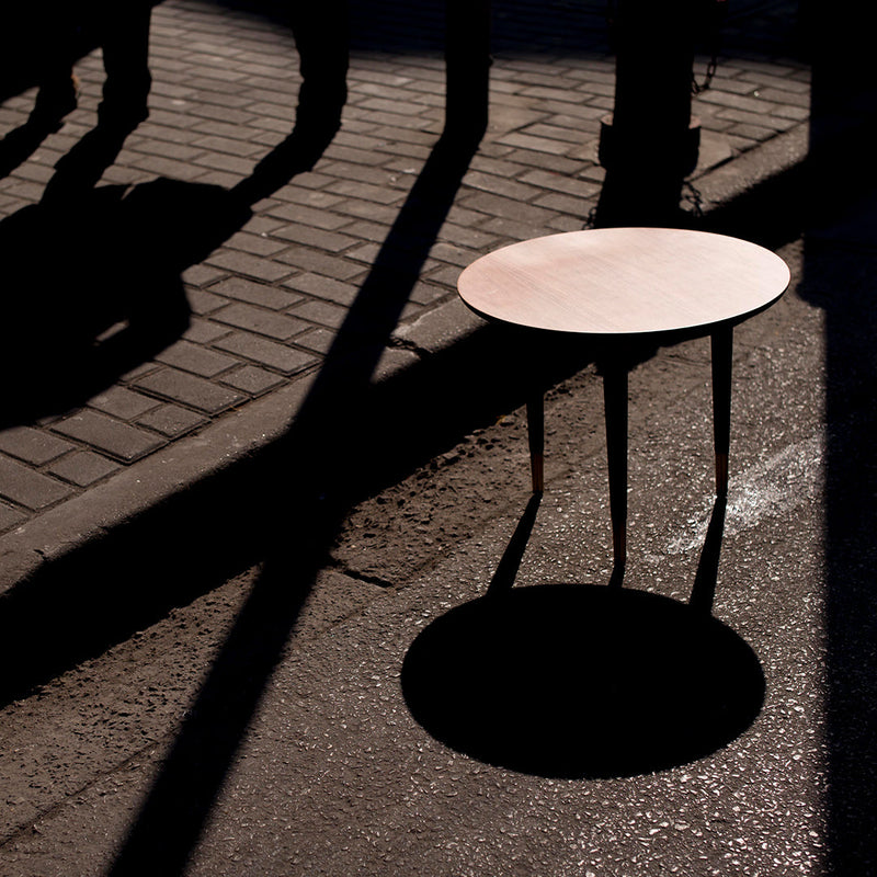 Minimalist round table in soft pink shade casting a distinct shadow on a textured pavement.