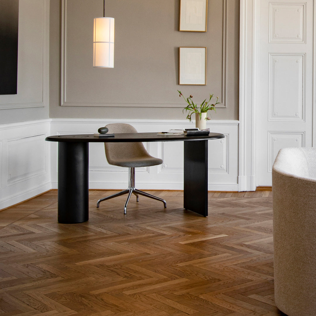 Modern black desk and sleek gray chair on rich wooden herringbone floor, with soft beige decor accents.