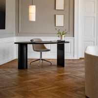 Modern black desk and sleek gray chair on rich wooden herringbone floor, with soft beige decor accents.