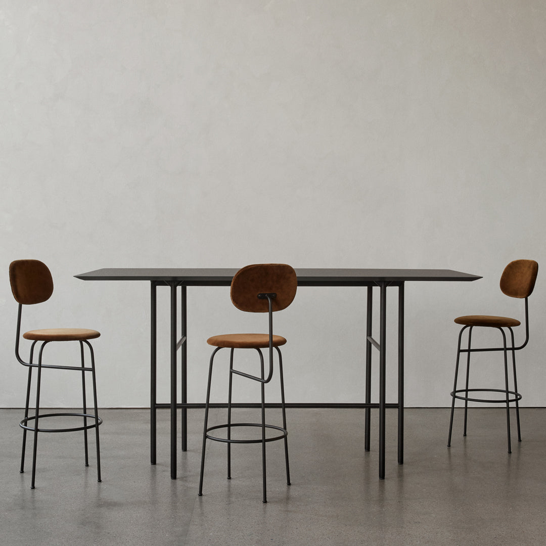 Modern black table with sleek lines and four tan upholstered bar stools in a minimalist setting.