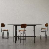 Modern black table with sleek lines and four tan upholstered bar stools in a minimalist setting.