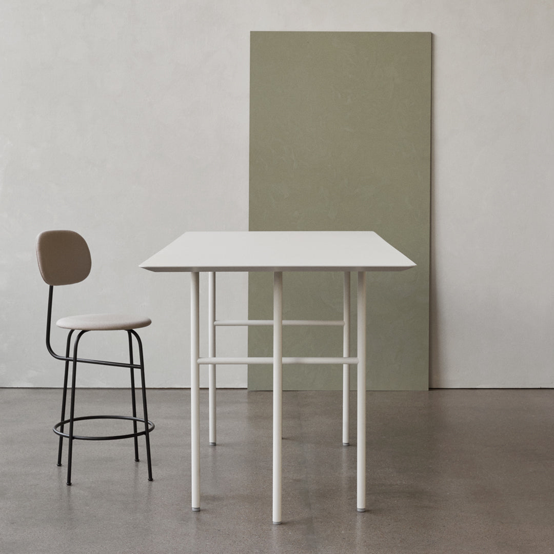 White table with minimalist design, paired with a beige chair against a muted green backdrop.