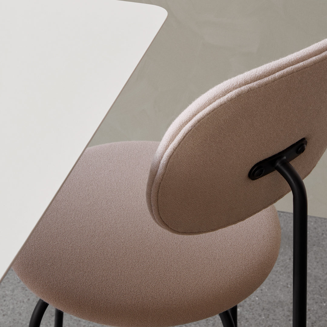 "Soft beige chair with a rounded back, paired with a sleek white table against a muted gray backdrop."