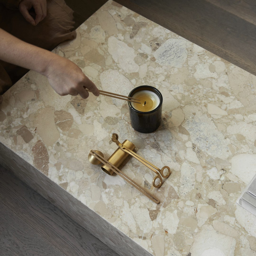 "Black candle holder on beige speckled stone surface, with gold-colored candle snuffer, creating a chic, modern aesthetic."