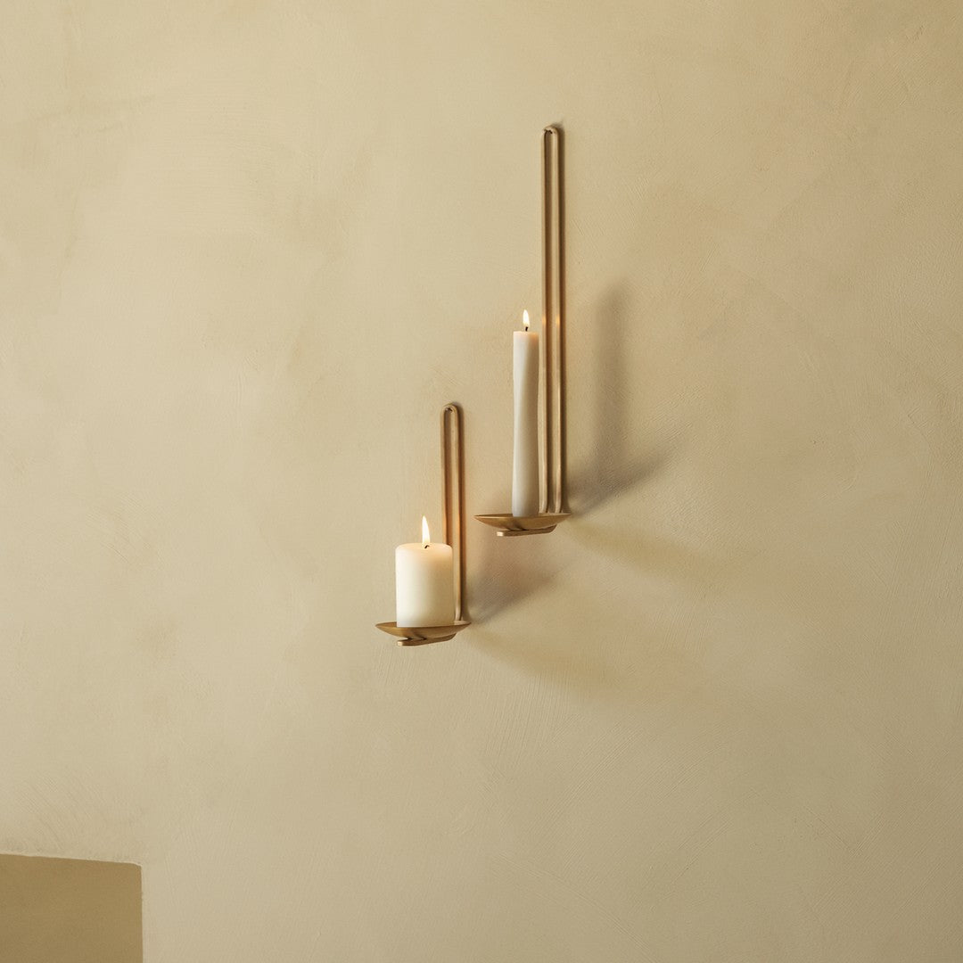 Gold wall sconces with white candles against a soft beige wall, creating an elegant, minimalist aesthetic.