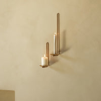 Gold wall sconces with white candles against a soft beige wall, creating an elegant, minimalist aesthetic.