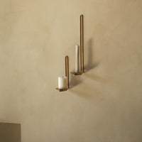 Gold candle holders against a smooth, neutral-toned wall with white candles. Elegant minimalist design.